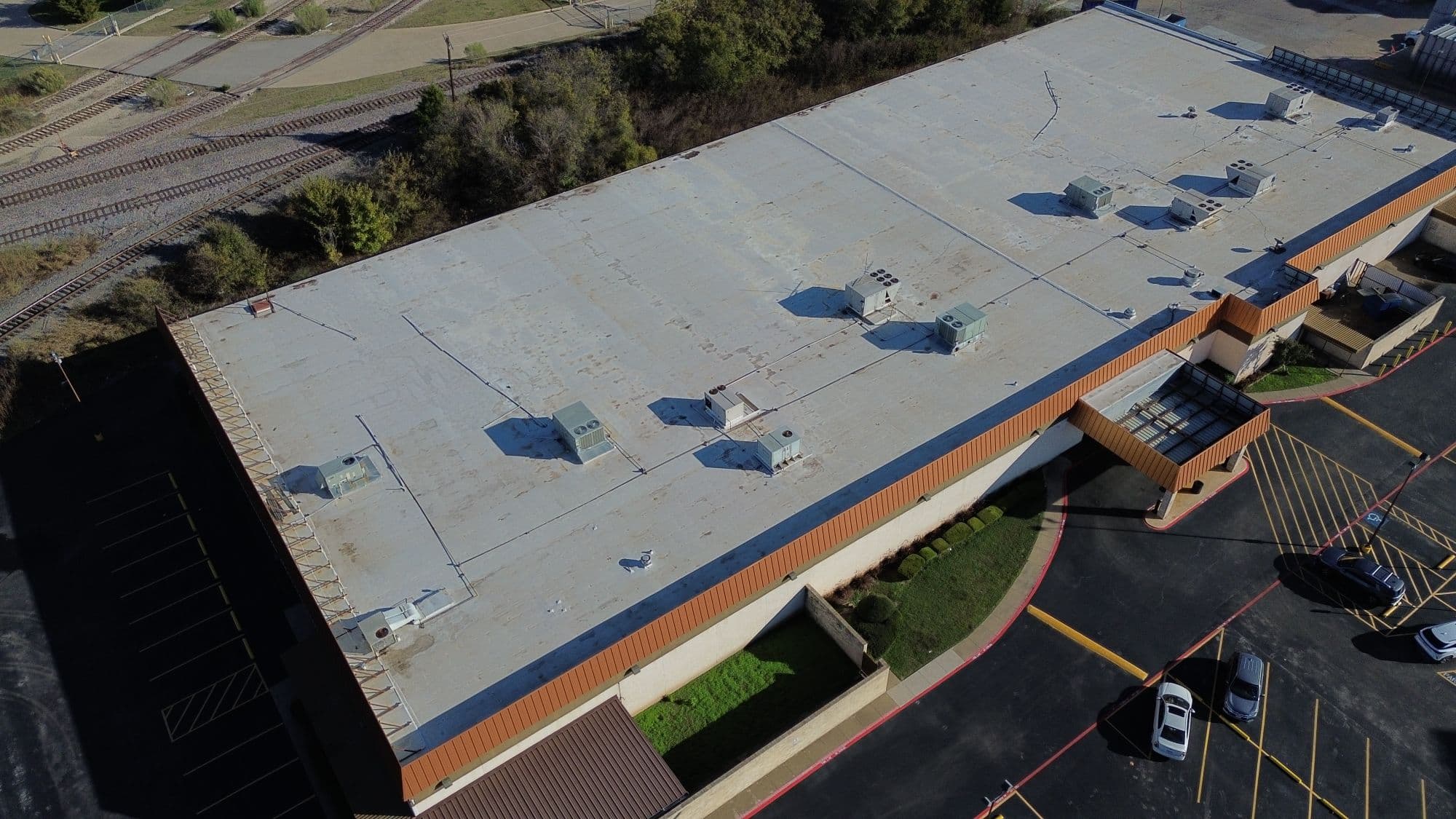 Aerial drone view of a large commercial strip center with orange facade — flat TPO roof with HVAC units