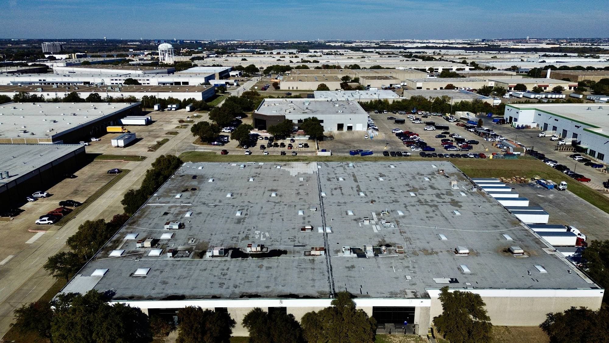 Wide aerial drone view of a massive commercial industrial complex spanning hundreds of thousands of square feet — DFW metro skyline in background
